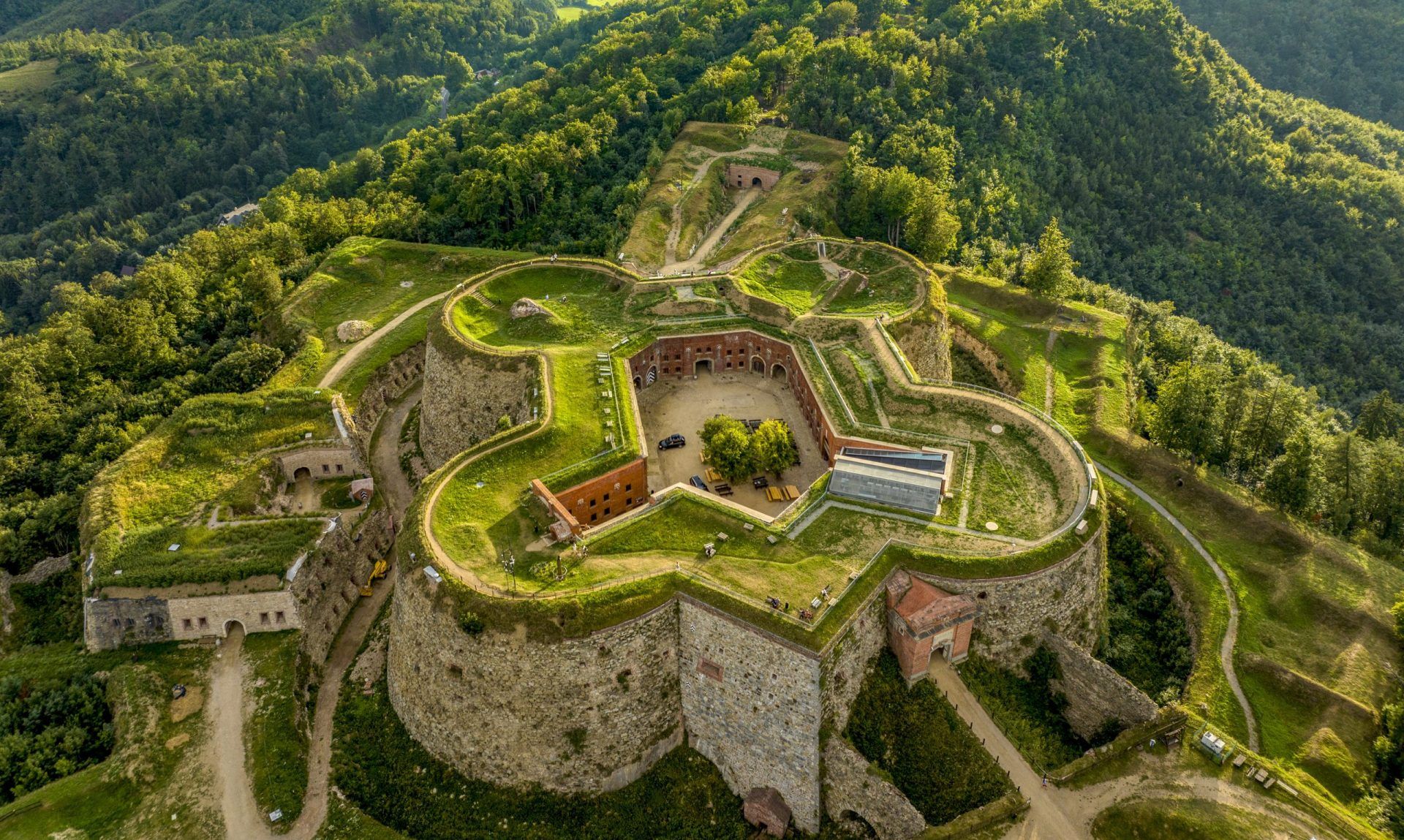 Majestatyczna twierdza górska na tle gór porośniętych gęstymi zielonymi lasami.