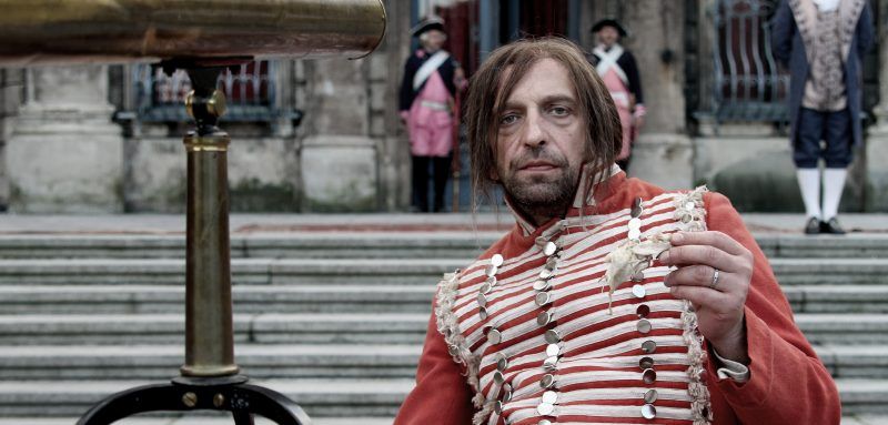 Główny bohater filmu siedzący na schodach ubrany w strój kostiumowy.