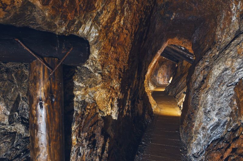 Lekko mroczny tunel wydrążony w skale. Na końcu korytarza lekkie światło, miejscami drewniane elementy.
