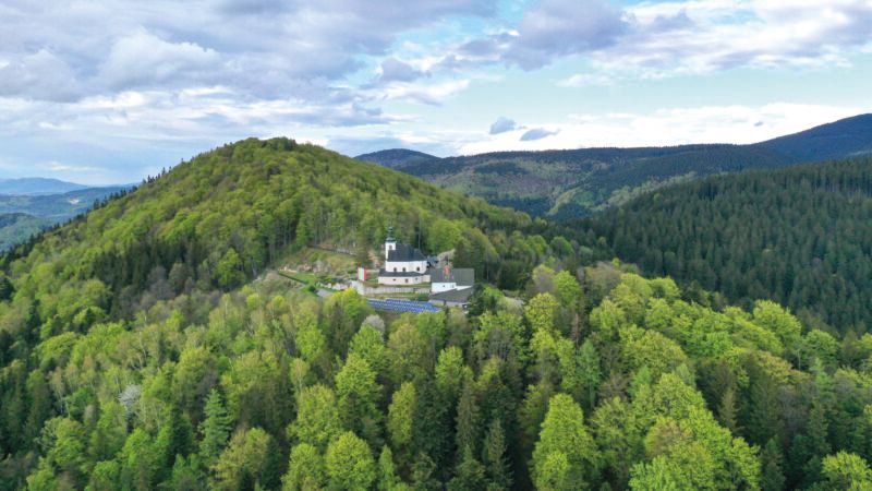 Widok z lotu ptaka na położone na zboczu góry zabytkowe sanktuarium w otoczeniu zielonych koron drzew i gór