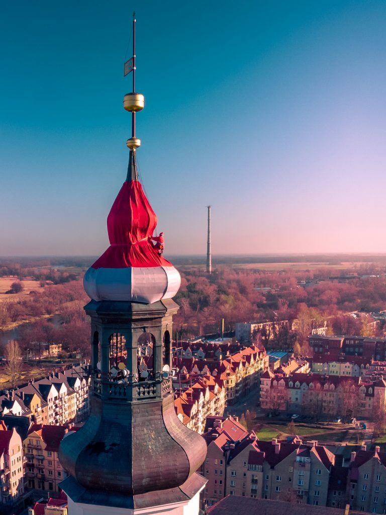 Widok z lotu ptaka na centrum Głogowa z wieżą ratuszową widoczną na pierwszym planie na tle błękitnego nieba