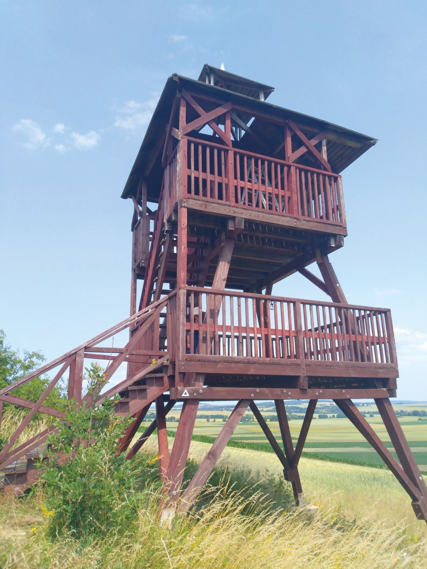 Widok na drewnianą, dwupoziomową, zadaszoną wieżę widokową położoną na zboczach niewielkiego wzniesienia