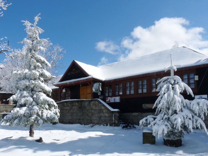 Widok na wejście do murowano-drewnianego schroniska do którego prowadzi trójkątna a