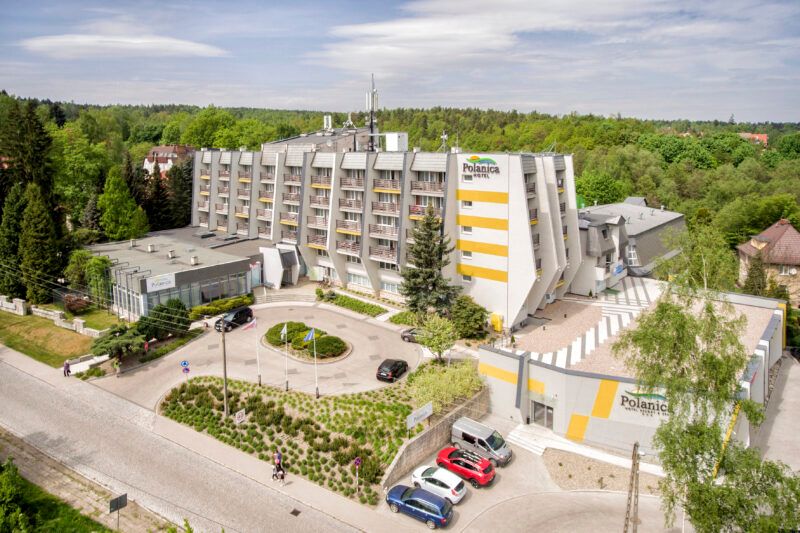 Zdjęcie wykonane z drona, przedstawia masywny, wielopiętrowy budynek hotelowy z podjazdem i parkingiem