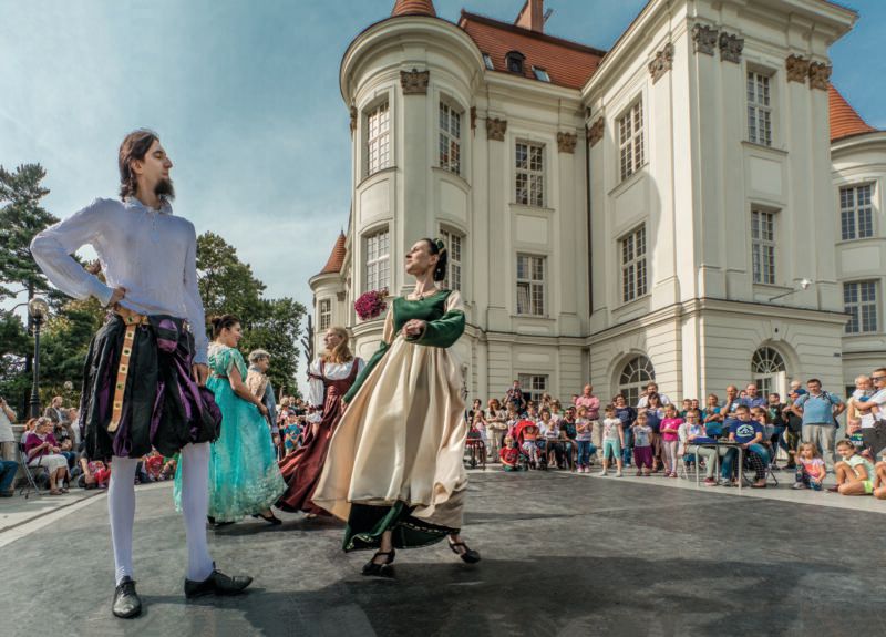 Tancerze na scenie w ludowych strojach na tle zamku i widzów