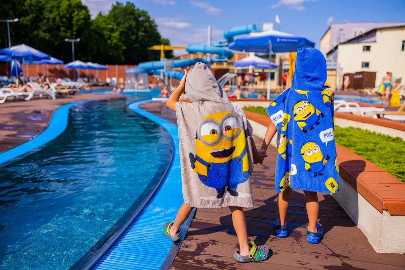 Goście basenu przykryci kolorowymi ręcznikami stoją przy basenie