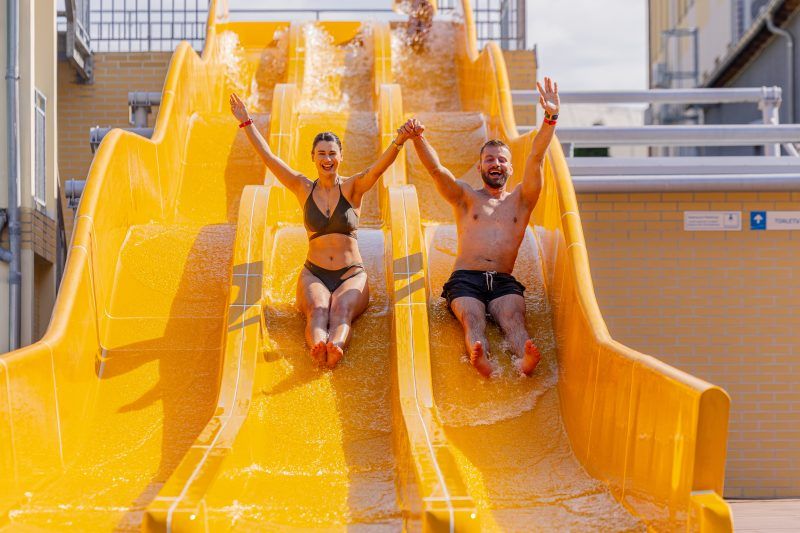 Żółta zjeżdzalnia a na niej dwie osoby podczas ślizgu