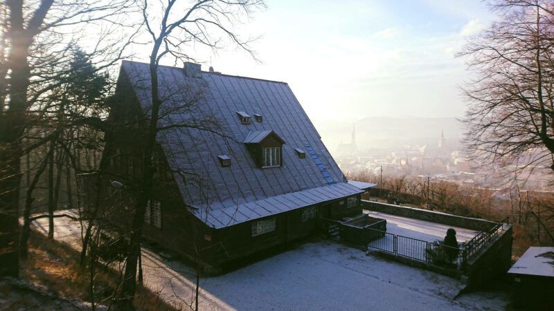 Widok z góry na dom turysty, dach pokryty śniegiem, wokół pozbytych drzew liści.