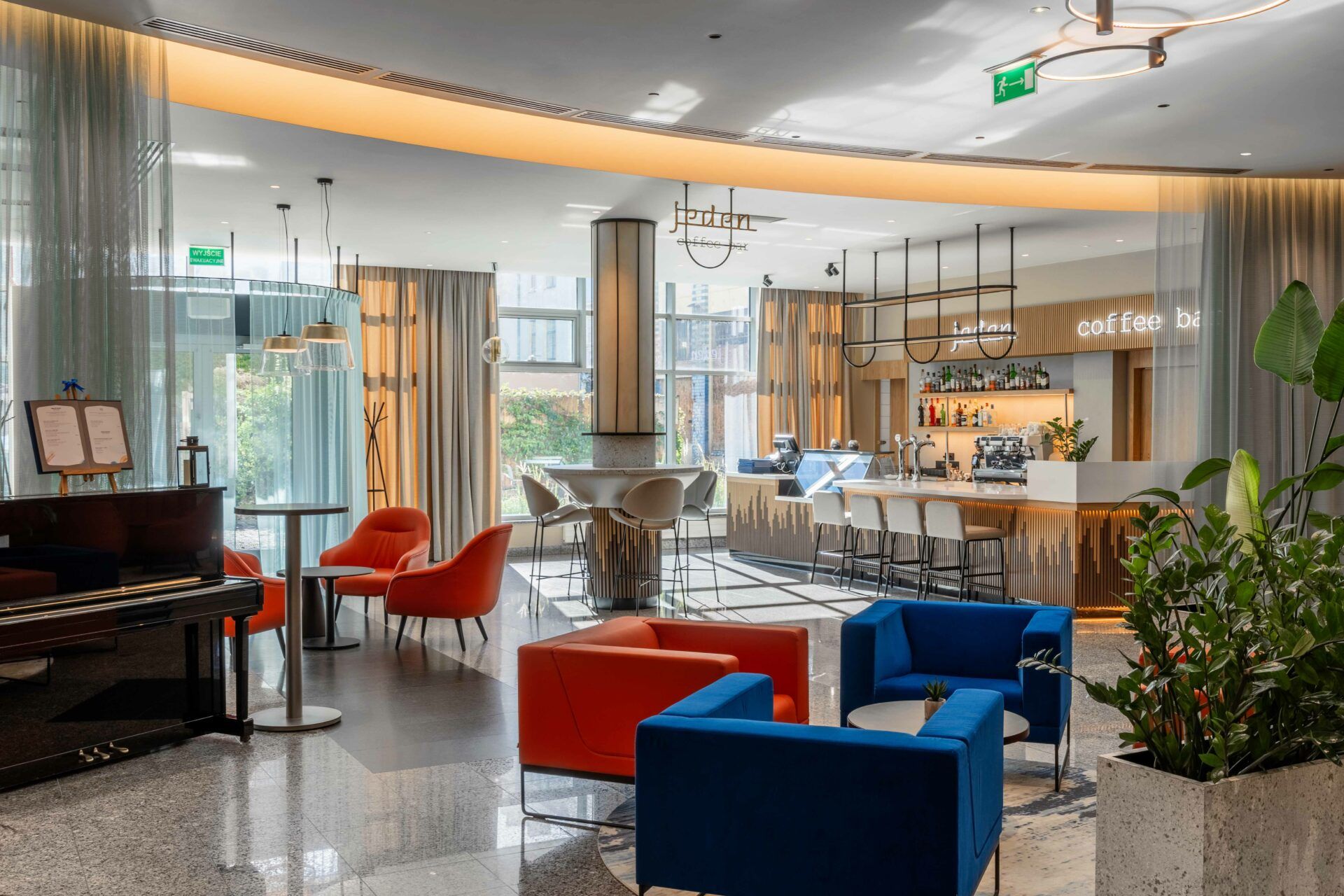 Nowoczesne lifestylowe wnętrze restauracji i baru. Pomieszczenie dobrze doświetlone, ma dużo elementów ozdobnych, rośliny w dużych donicach, pianino, kolorowe sofy, neonowe napisy.