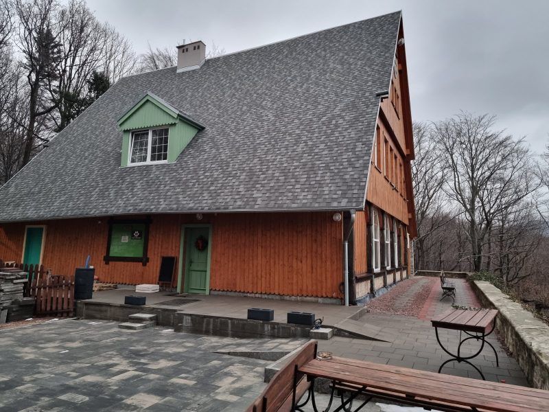 zdjęcie wykonane zimą zrobione od boku, z bliska na bordowy budynek, będący schroniskiem.