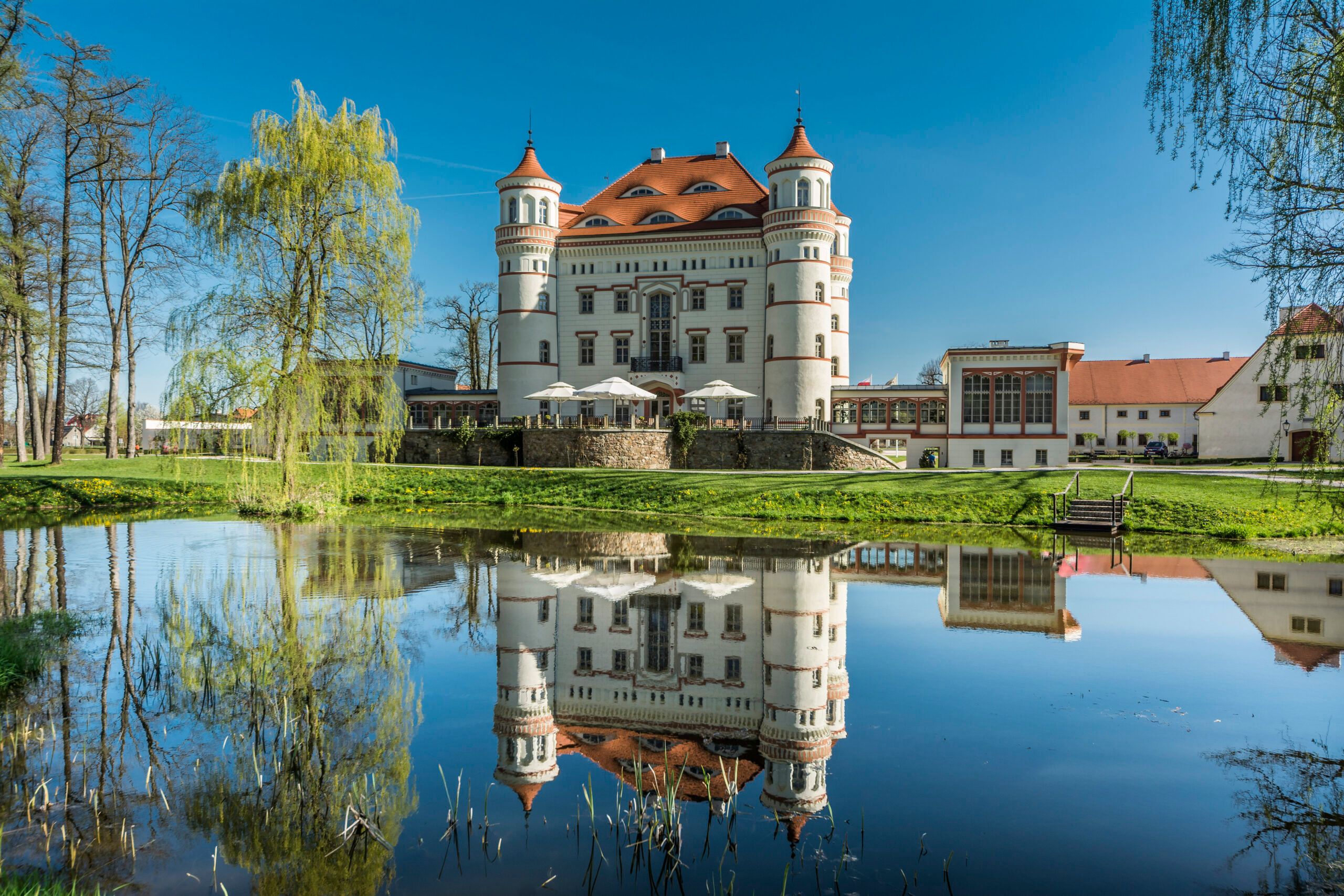 Widok od strony stawu na budynek pałacu Wojanów na tle błękitnego nieba
