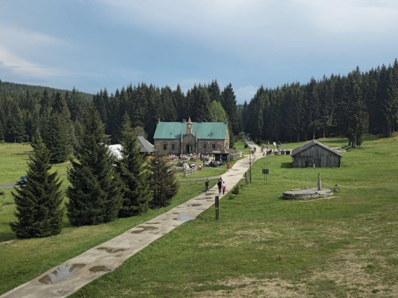 zdjęcie przedstawia drogę do schroniska otoczoną polami, na końcu drogi znajduję się schronisko z zielonym dachem