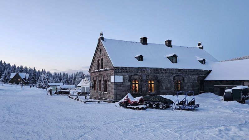 zdjęcie wykonane zimą przedstawia drewniane schronisko podczas wschodu słońca