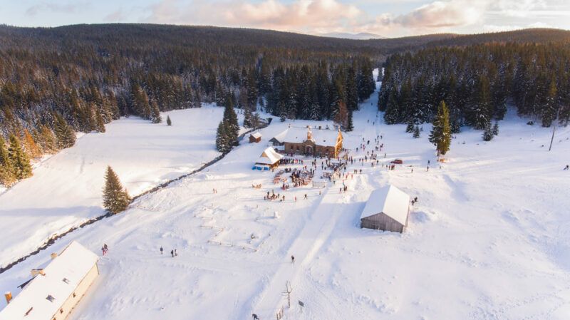 widok z lotu ptaka na ogromne ośnieżone pole na którego terenie znajduje się obiekt. w tle znajduję się las