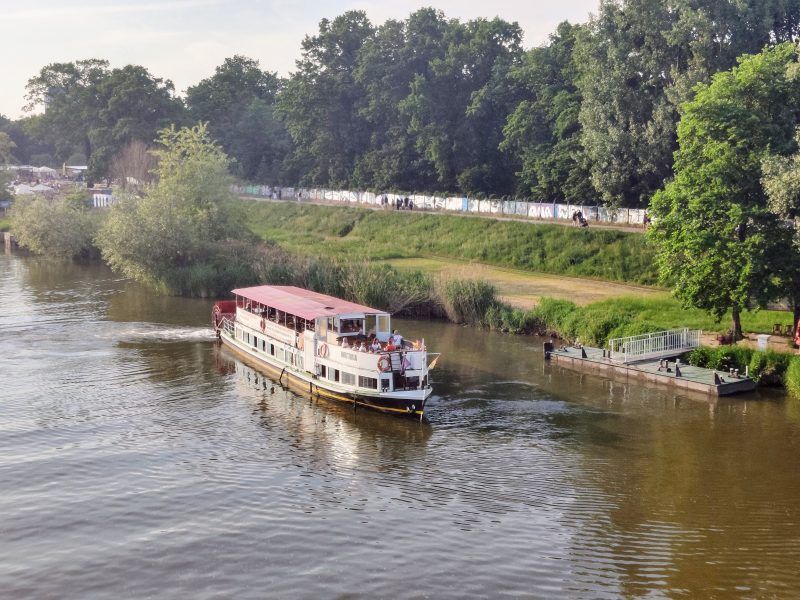 widok znad rzeki na przystań na brzegu do której dopływa katamaran