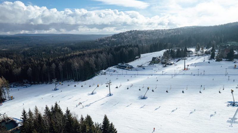 Równo ośnieżony stok narciarski przecinany wyciągami.