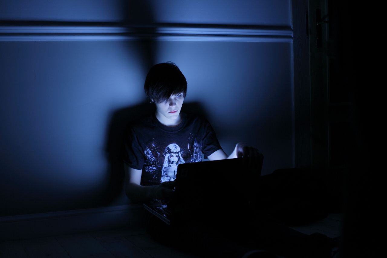 Zdjęcie przedstawia kadr z filmu Sala Samobójców z mężczyzną spoglądającym na monitor laptopa w zaciemnionym pokoju