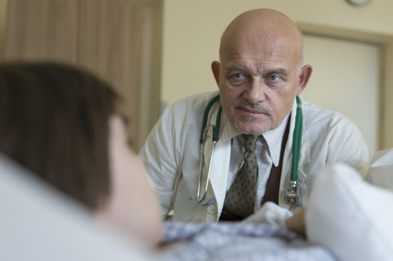 Doktor obserwujący chłopca leżącego na łóżku szpitalnym.