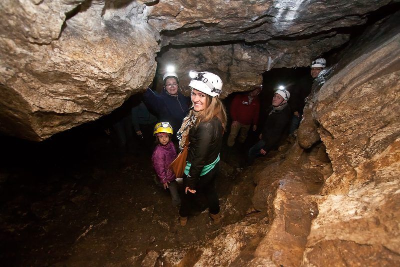 Grupa turystów z kobietą i dziećmi spoglądającymi w kadr na trasie turystycznej w Jaskini Radochowskiej