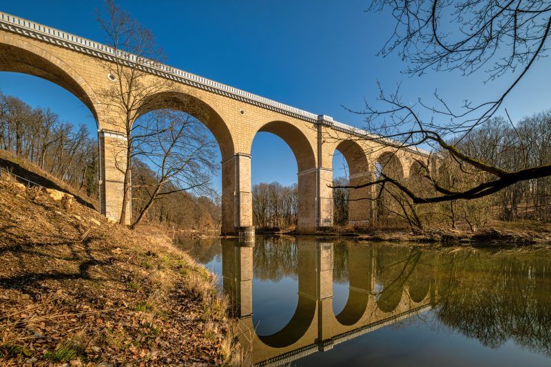 Zdjęcie przedstawia monumentalny, kamienny most kolejowy w Zgorzelcu o łukowej konstrukcji, który wznosi się nad Nysą Łużycką