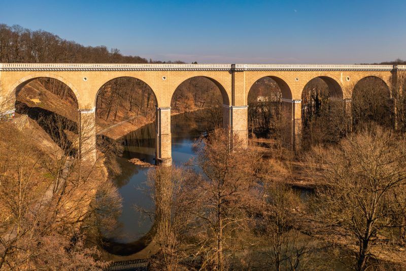 Zdjęcie przedstawia monumentalny, kamienny most kolejowy w Zgorzelcu o łukowej konstrukcji, który wznosi się nad Nysą Łużycką