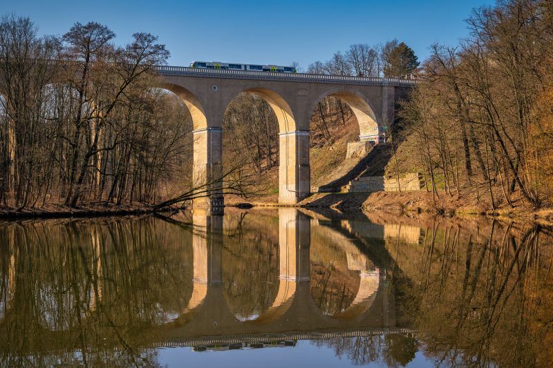 Zdjęcie przedstawia monumentalny, kamienny most kolejowy w Zgorzelcu o łukowej konstrukcji, który wznosi się nad Nysą Łużycką