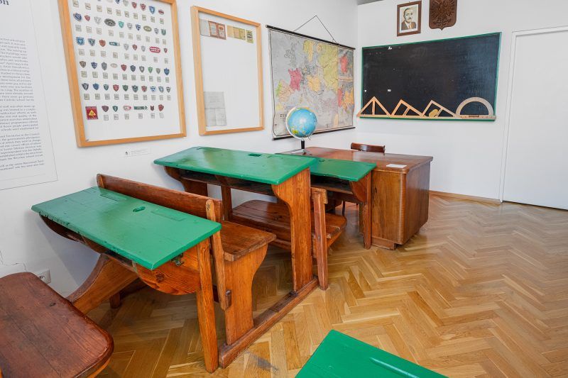 Zdjęcie przedstawia stare, drewniane ławy szkolne ustawione w klasie