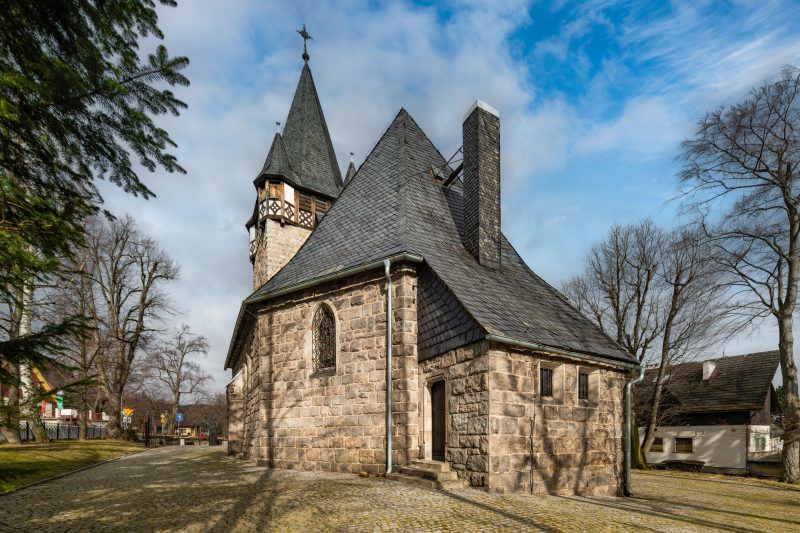 Neogotycka świątynia z ciemnego granitu, z wysoką wieżą i stromym dachem pokrytym łuskową blachą.