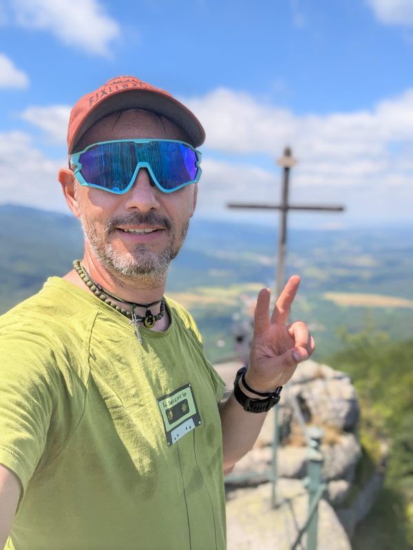 Zdjęcie twarzy mężczyzny spoglądającego w kadr na tle Krzyża stojącego na szczycie góry