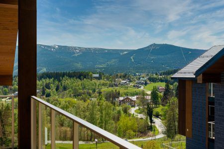 Malowniczą panoramA Szklarskiej Poręby z widokiem na pasmo Karkonoszy widziana z tarasu Happy Valley Resort . W tle widać Śnieżne Kotły oraz charakterystyczną górę Szrenicę, co podkreśla górski, wypoczynkowy charakter miejsca.