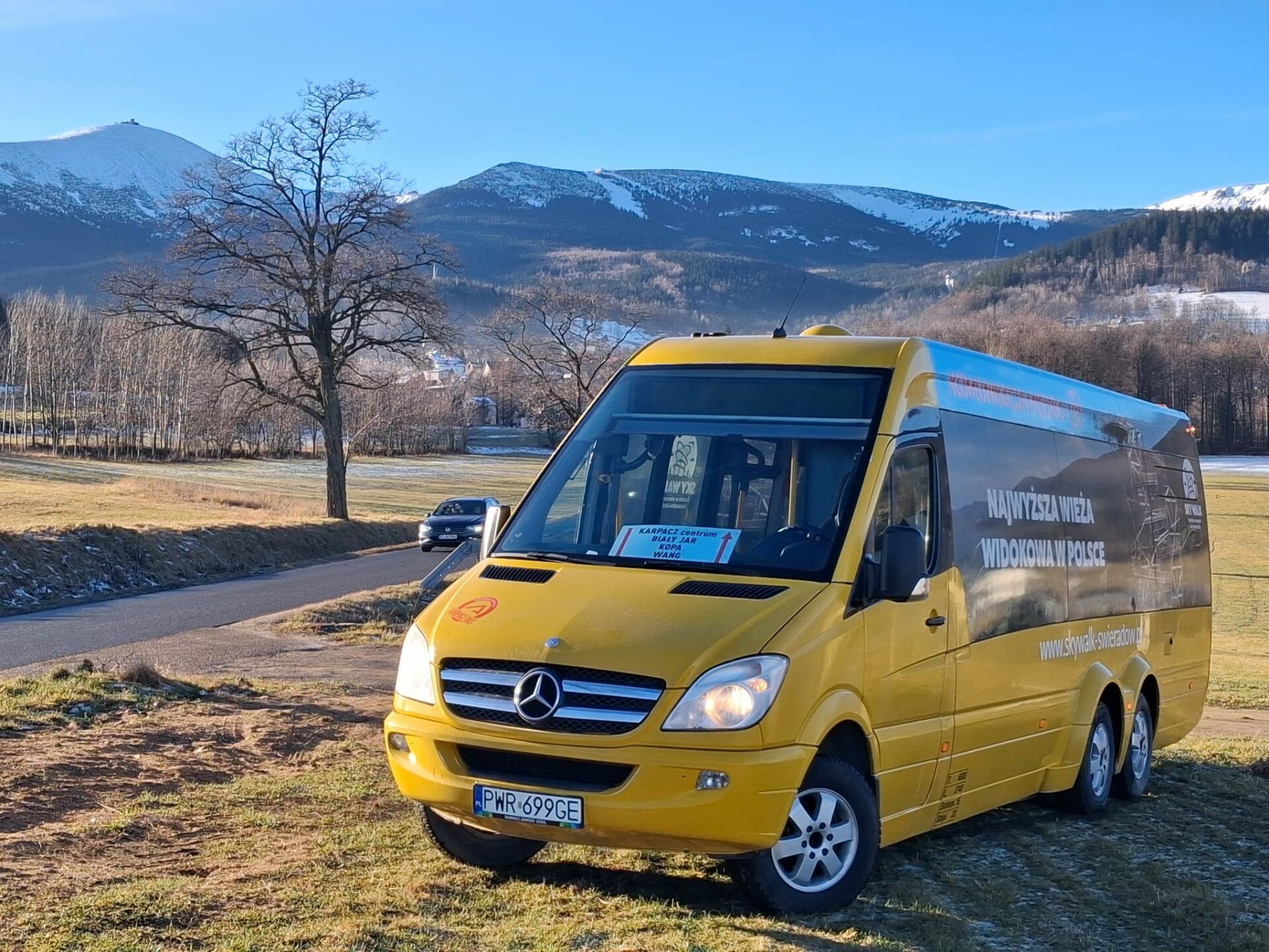 Żółty autobus firmy Vip Travel na tle jesiennej panoramy Karkonoszy