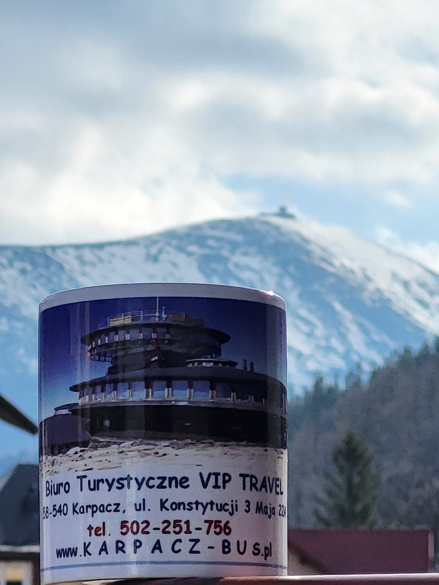 Zdjęcie ośnieżonego szczytu Śnieżki z kubkiem z reklamą biura turystycznego VIP Travel