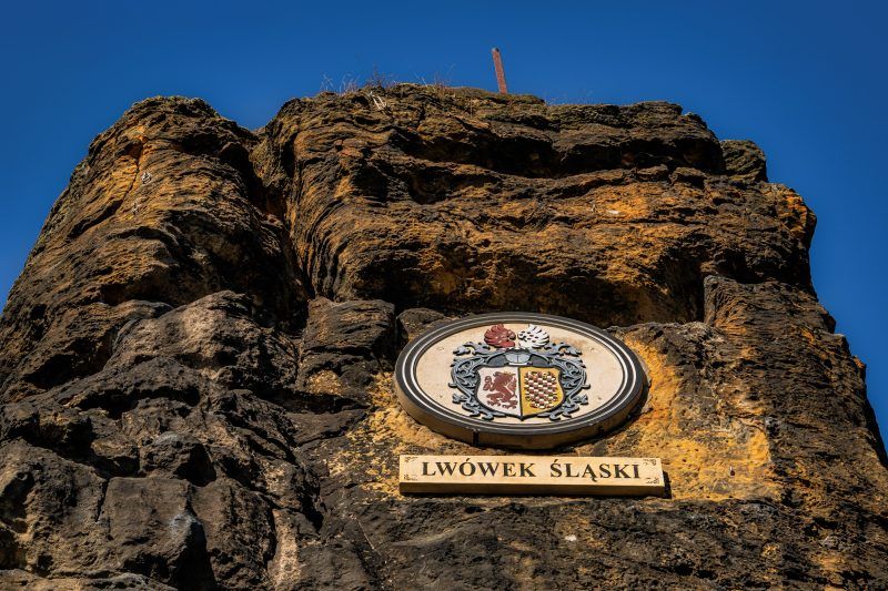 Na zdjęciu widać majestatyczną, 14-metrową piaskowcową skałę, wznoszącą się samotnie na tle zielonego krajobrazu. U jej południowego zbocza znajduje się medalion z wizerunkiem cesarza Wilhelma I, a w górnej części, mimo upływu lat, zachowały się ślady po metalowych barierkach i maszcie, które kiedyś służyły jako punkt widokowy.