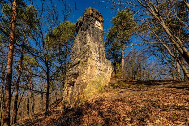 Na zdjęciu widać majestatyczną, 14-metrową piaskowcową skałę, wznoszącą się samotnie na tle zielonego krajobrazu. U jej południowego zbocza znajduje się medalion z wizerunkiem cesarza Wilhelma I, a w górnej części, mimo upływu lat, zachowały się ślady po metalowych barierkach i maszcie, które kiedyś służyły jako punkt widokowy.