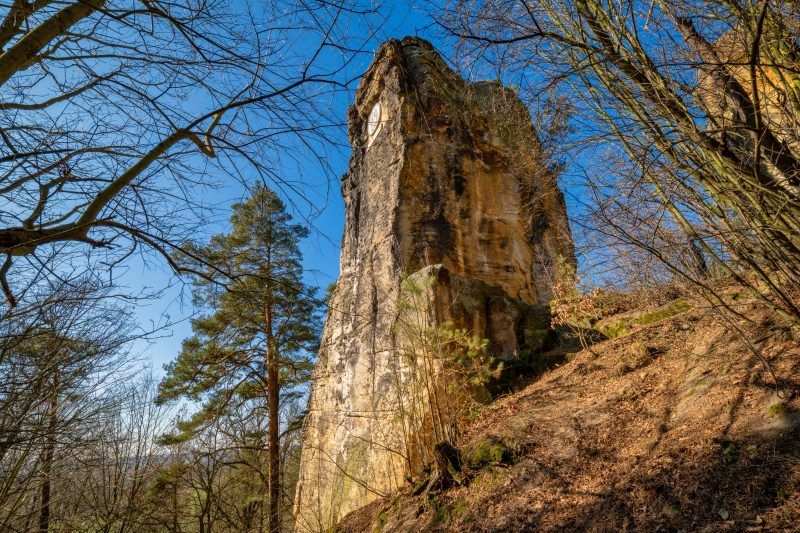 Na zdjęciu widać majestatyczną, 14-metrową piaskowcową skałę, wznoszącą się samotnie na tle zielonego krajobrazu. U jej południowego zbocza znajduje się medalion z wizerunkiem cesarza Wilhelma I, a w górnej części, mimo upływu lat, zachowały się ślady po metalowych barierkach i maszcie, które kiedyś służyły jako punkt widokowy.