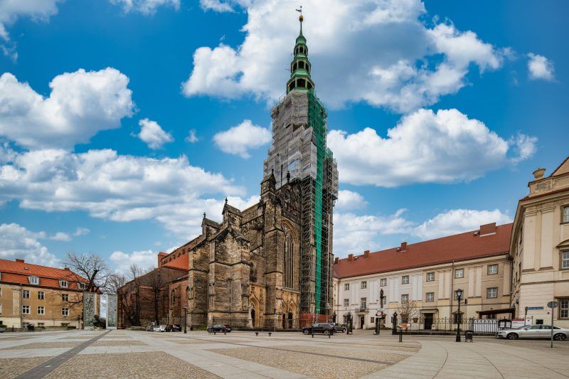 imponująca budowla z wysokimi, strzelistymi wieżami, których szczyty sięgają nieba, a na tle nieba wyróżnia się gotycka fasada, ozdobiona bogatymi detalami i witrażami, z majestatycznymi przyporami podpierającymi mur.