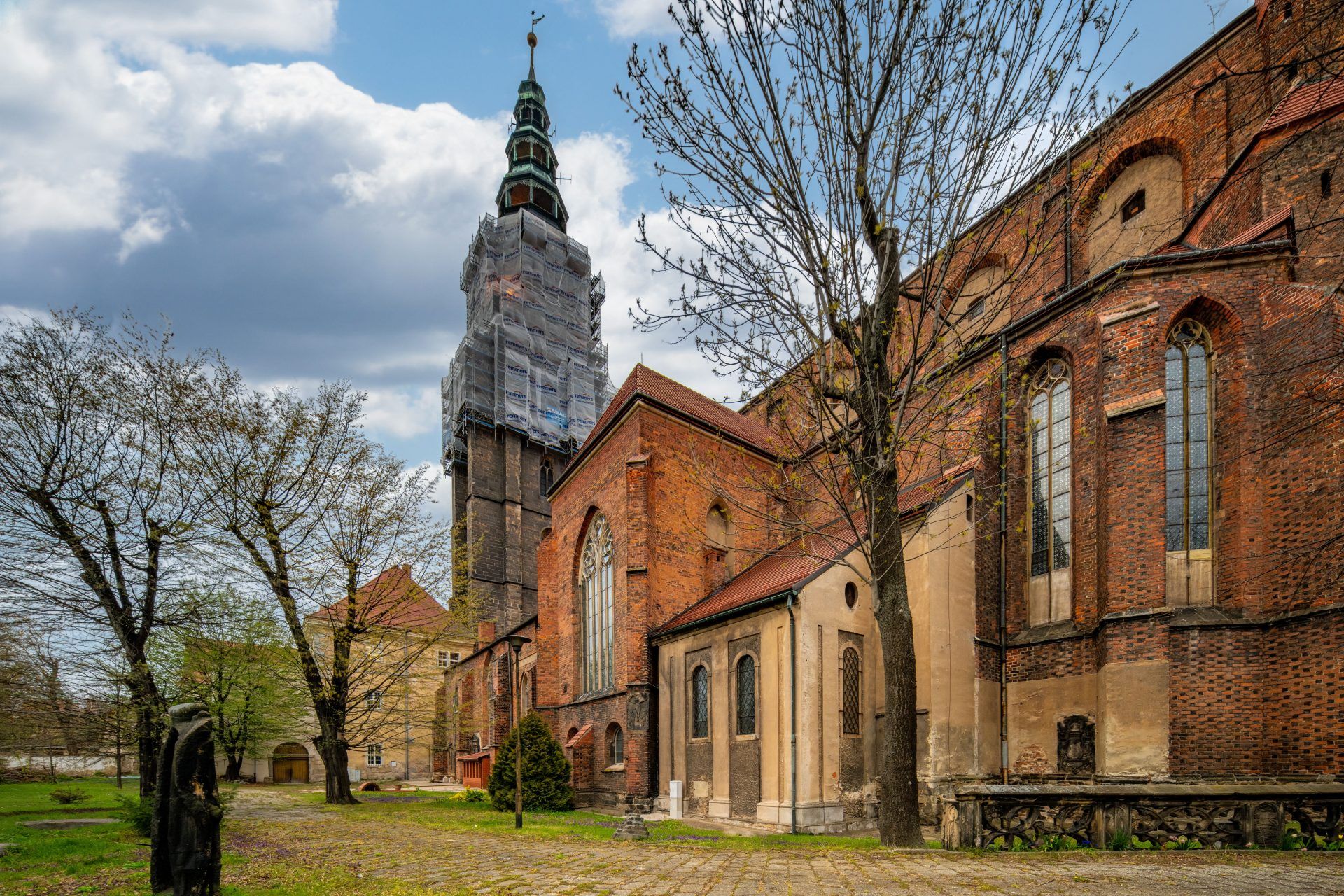 Imponująca budowla z wysokimi, strzelistymi wieżami, których szczyty sięgają nieba, a na tle nieba wyróżnia się gotycka fasada, ozdobiona bogatymi detalami i witrażami, z majestatycznymi przyporami podpierającymi mur.