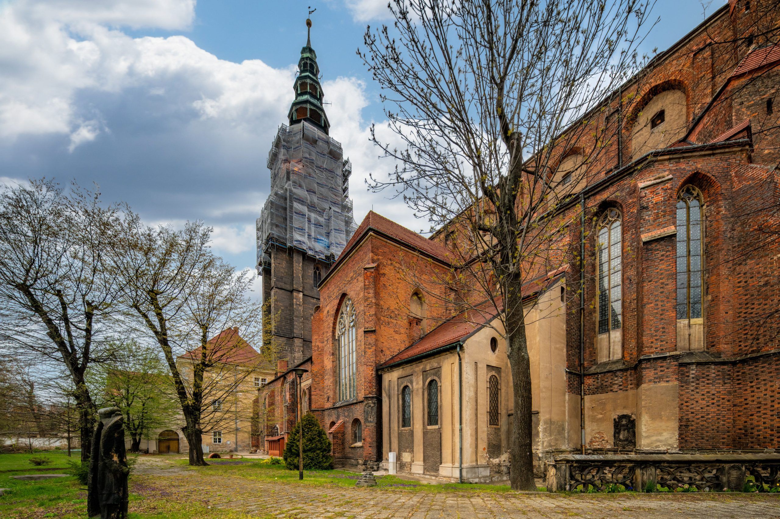 Imponująca budowla z wysokimi, strzelistymi wieżami, których szczyty sięgają nieba, a na tle nieba wyróżnia się gotycka fasada, ozdobiona bogatymi detalami i witrażami, z majestatycznymi przyporami podpierającymi mur.