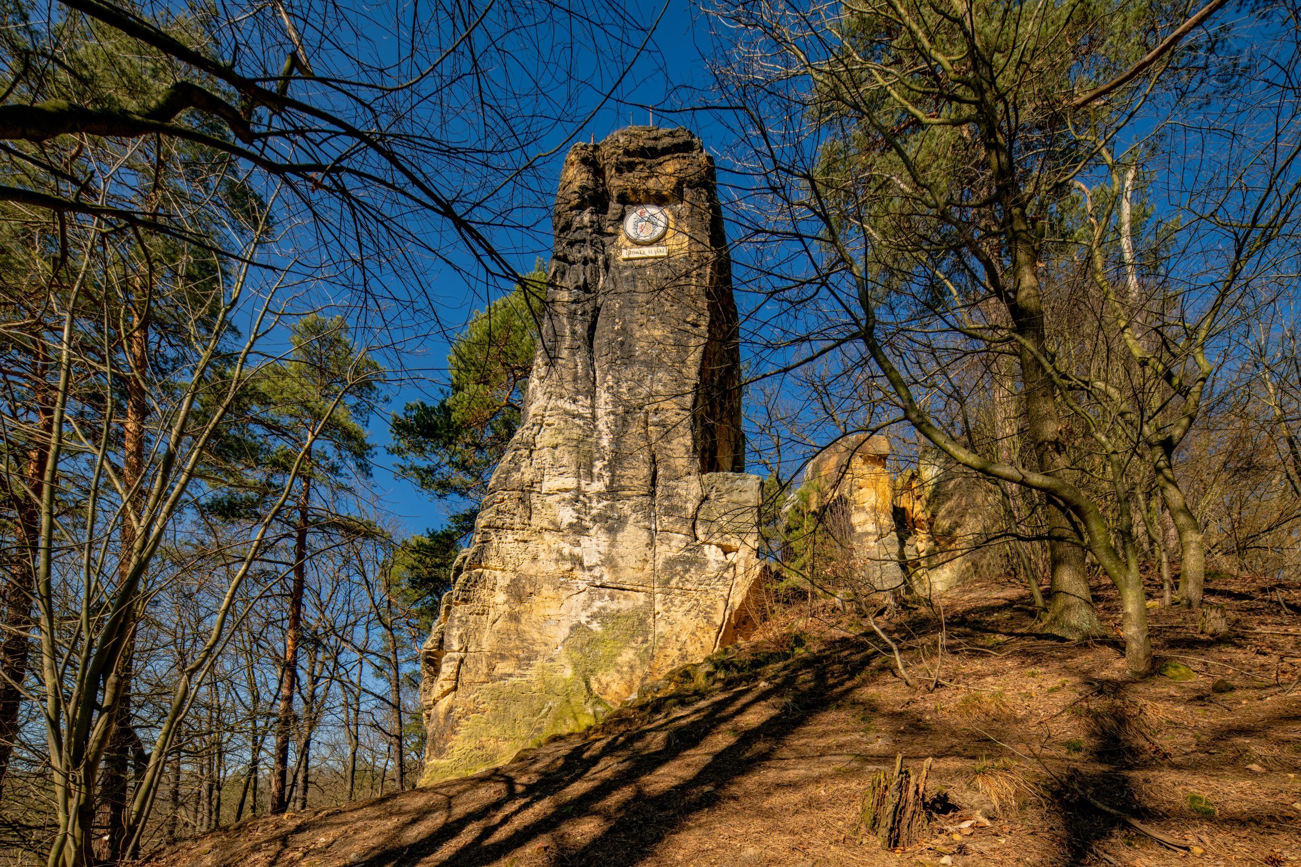 Na zdjęciu widać majestatyczną, 14-metrową piaskowcową skałę, wznoszącą się samotnie na tle zielonego krajobrazu. U jej południowego zbocza znajduje się medalion z wizerunkiem cesarza Wilhelma I, a w górnej części, mimo upływu lat, zachowały się ślady po metalowych barierkach i maszcie, które kiedyś służyły jako punkt widokowy.
