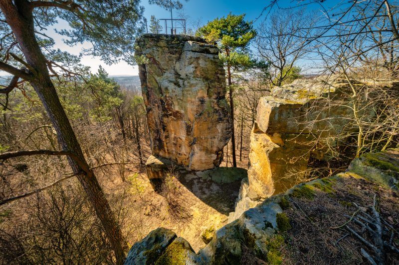 Na zdjęciu widać majestatyczną, 14-metrową piaskowcową skałę, wznoszącą się samotnie na tle zielonego krajobrazu. U jej południowego zbocza znajduje się medalion z wizerunkiem cesarza Wilhelma I, a w górnej części, mimo upływu lat, zachowały się ślady po metalowych barierkach i maszcie, które kiedyś służyły jako punkt widokowy.