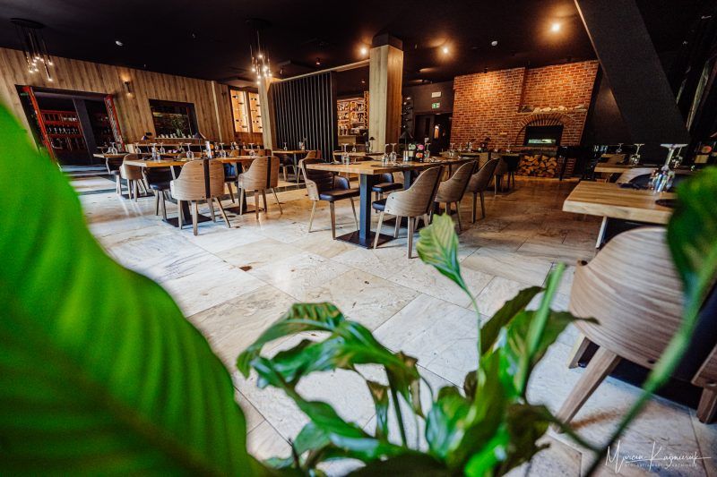 Elegancka sala restauracyjna z designerskim oświetleniem i drewnianymi akcentami. Przestrzeń zachęca do spokojnych posiłków w przytulnej atmosferze.