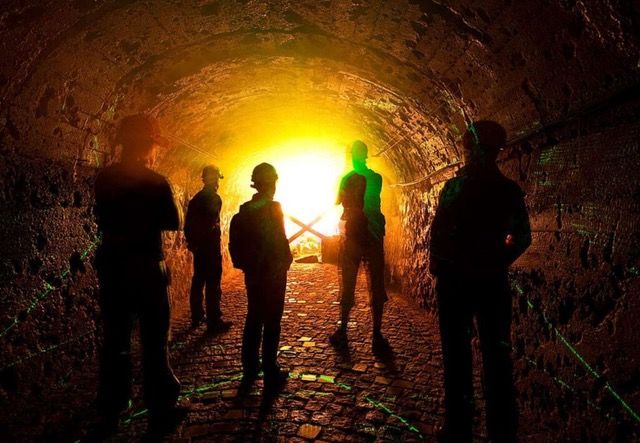 Grupa osób stoi w sztolni naprzeciwko dużego źródła światła