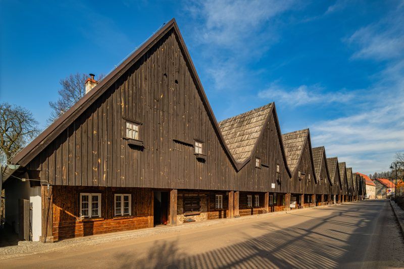 Drewniane domki Dwunastu Apostołów w Chełmsku Śląskim tworzą urokliwy rząd o ciemnych, szachulcowych fasadach i stromych dachach, wznosząc się na tle czystego, błękitnego nieba.