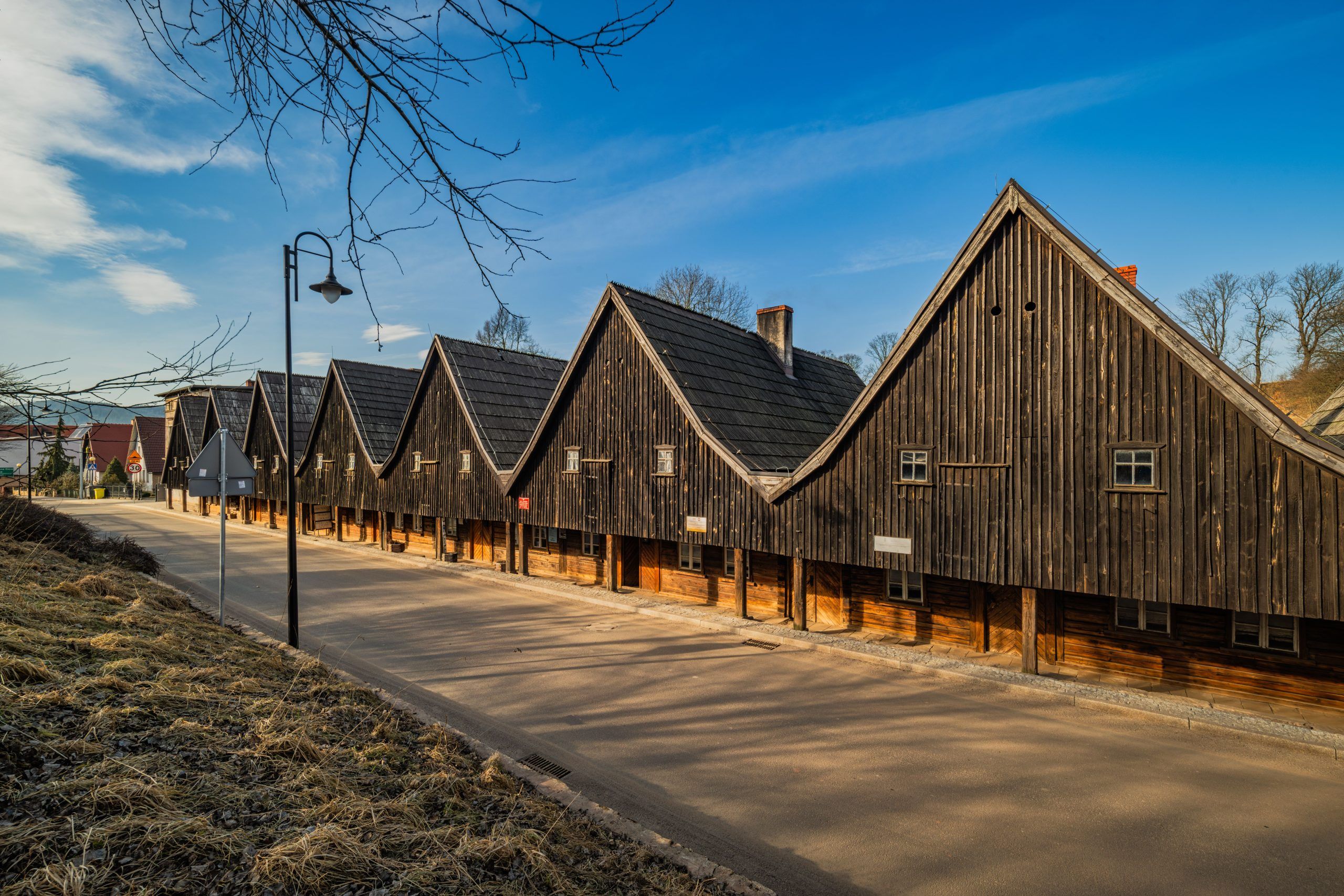 Drewniane domki Dwunastu Apostołów w Chełmsku Śląskim tworzą urokliwy rząd o ciemnych, szachulcowych fasadach i stromych dachach, wznosząc się na tle czystego, błękitnego nieba.