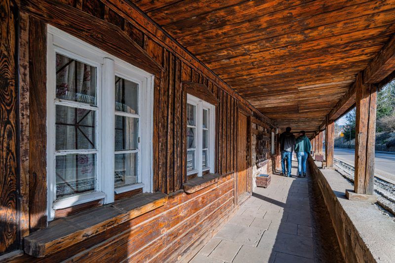 Drewniany podcień domków Dwunastu Apostołów w Chełmsku Śląskim, z białymi oknami i ciepłym odcieniem desek, prowadzi wzdłuż spokojnej ulicy.