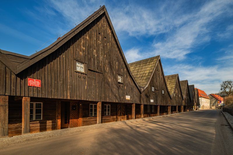 Drewniane domki Dwunastu Apostołów w Chełmsku Śląskim tworzą urokliwy rząd o ciemnych, szachulcowych fasadach i stromych dachach, wznosząc się na tle czystego, błękitnego nieba.