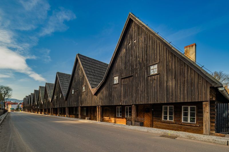 Drewniane domki Dwunastu Apostołów w Chełmsku Śląskim tworzą urokliwy rząd o ciemnych, szachulcowych fasadach i stromych dachach, wznosząc się na tle czystego, błękitnego nieba.