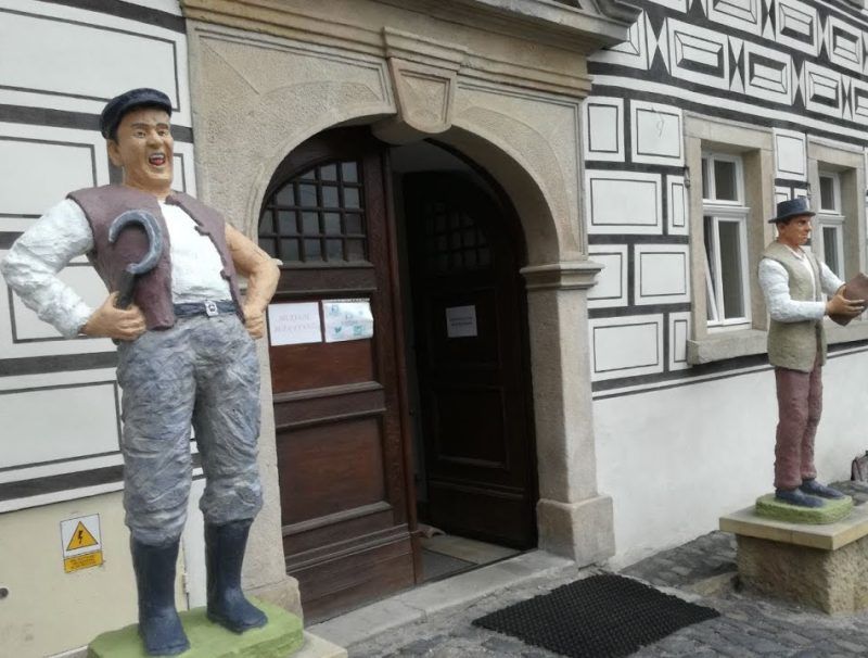 wejście do muzeum, po bokach drzwi stoją dwie wysokie figurki przedstawiające mężczyzn