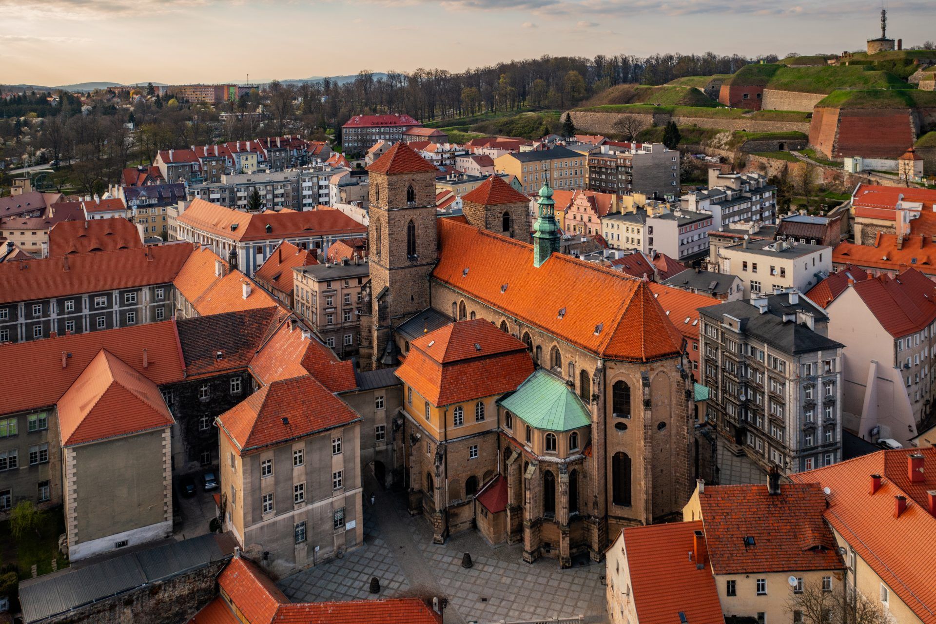 Gotycki kościół z czerwonej cegły i wysoką wieżą góruje nad gęstą zabudową kłodzkiej starówki.