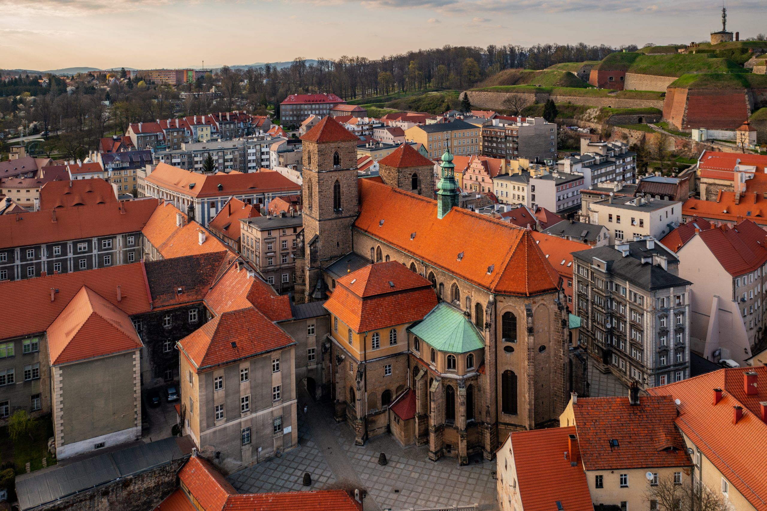 Gotycki kościół z czerwonej cegły i wysoką wieżą góruje nad gęstą zabudową kłodzkiej starówki.
